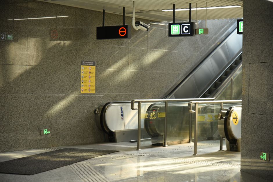 Interior view of a modern subway station featuring escalators and directional signage.