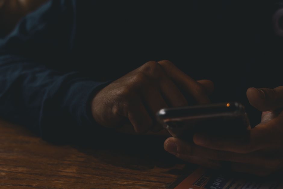 A close-up view of hands interacting with a smartphone in a dim indoor setting, highlighting technology use.