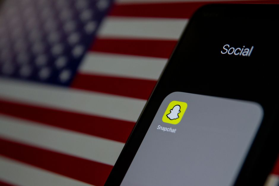 Close-up of a smartphone with Snapchat app icon, American flag in background.