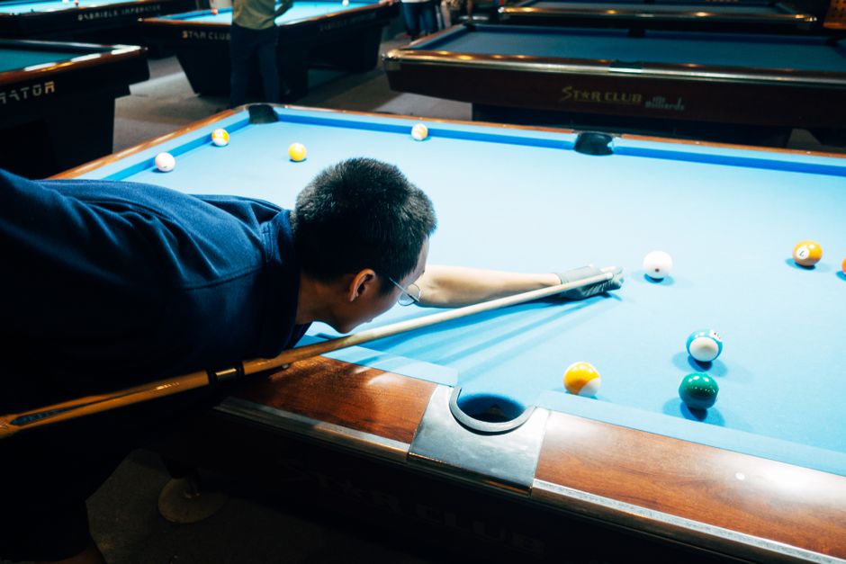 A man skillfully playing billiards, focusing on his shot on a pool table.