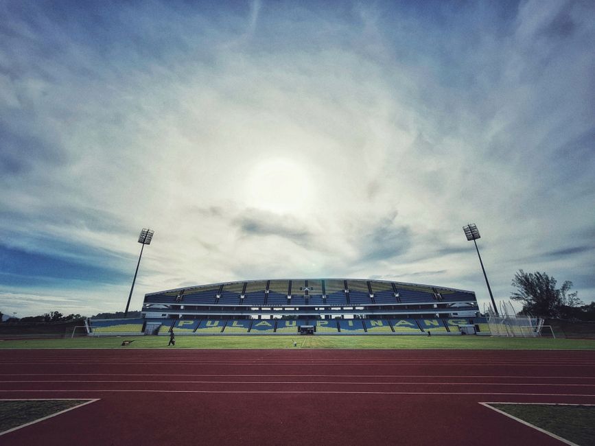 Wide-angle view of a football stadium with a running track under a dramatic cloudy sky creating a stunning visual.